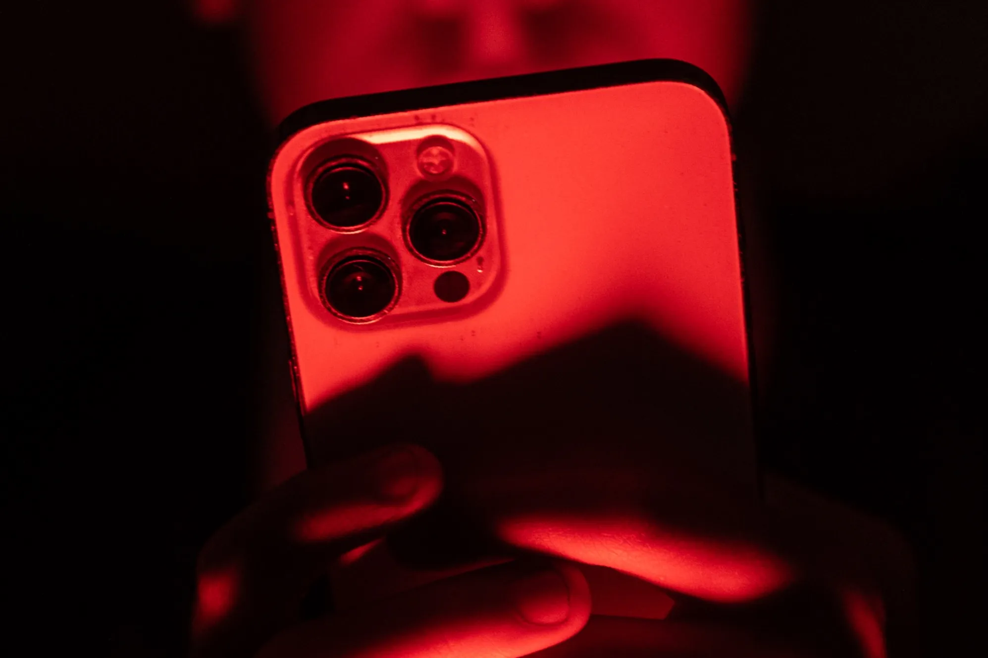 Persona sosteniendo un iPhone frente a fondo rojo