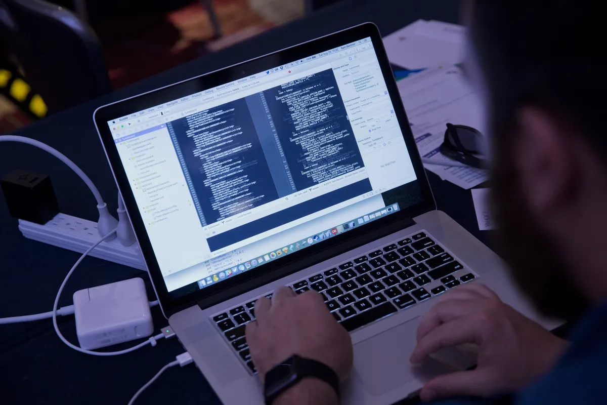 Ilustración de un hacker frente a varias pantallas con código, en referencia al uso de IA en ciberataques